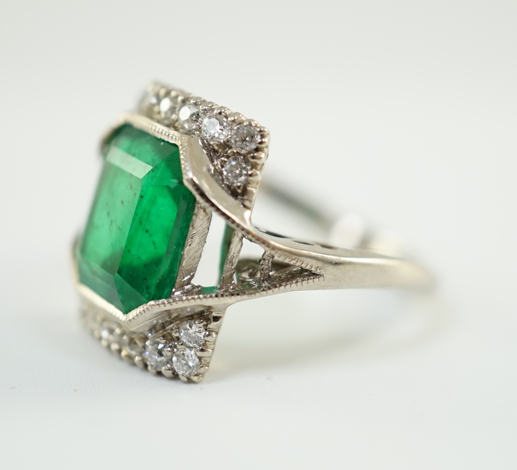 An Art Deco 18k white gold, emerald and diamond set square cluster dress ring, with shaped cut sapphire set shoulders, (a.f.)